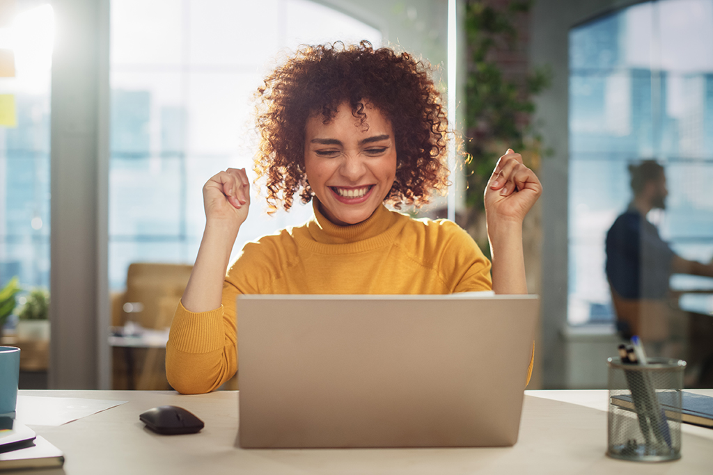 Happy woman sitting at desk and using laptop.