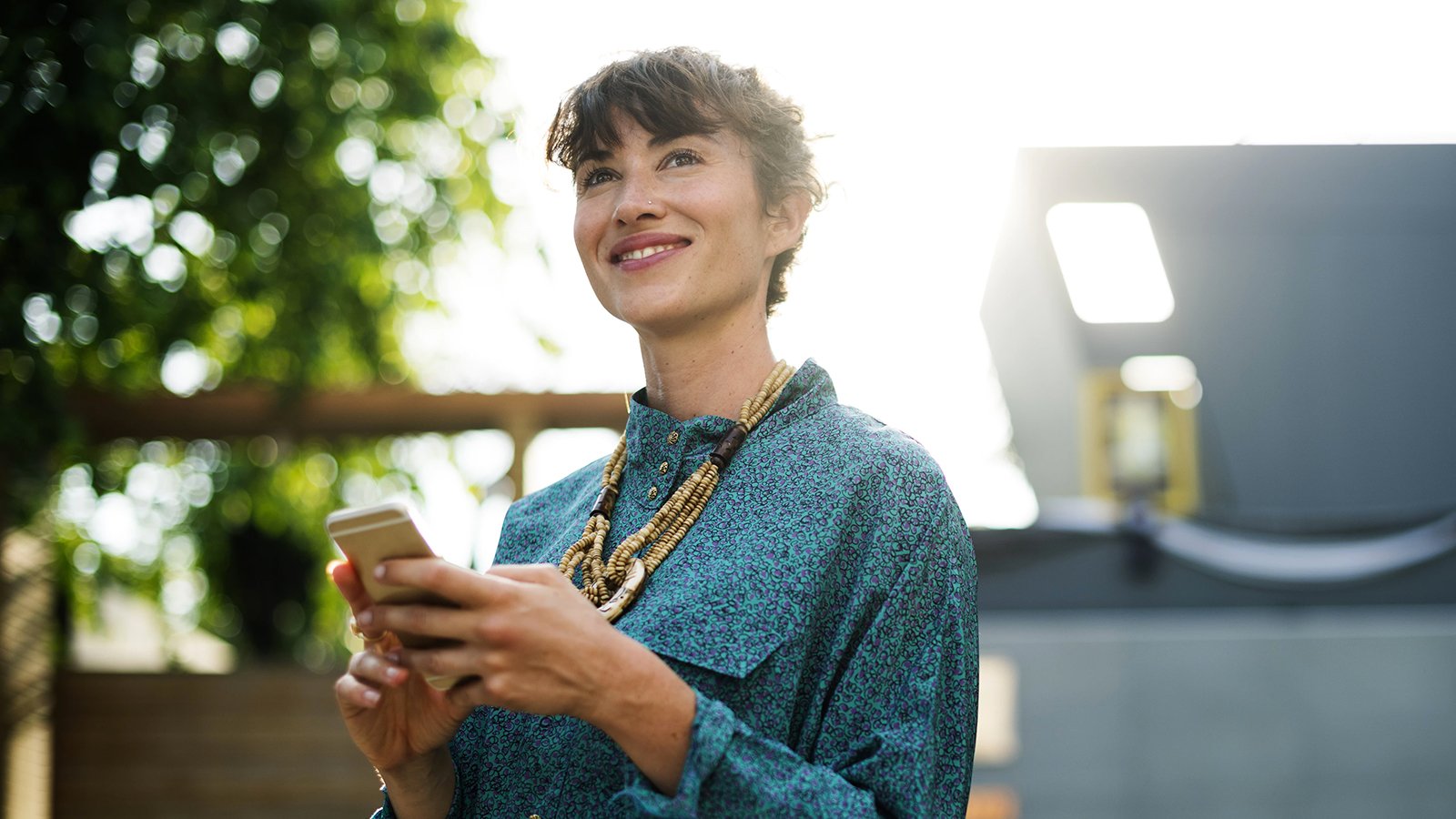 Happy woman holding smart phone and looking away with a big smile.