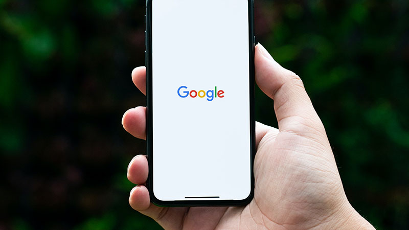 Hand holding mobile phone with Google Search on the screen.